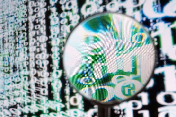 A magnifying glass held against a computer screen enlarges lines of code.