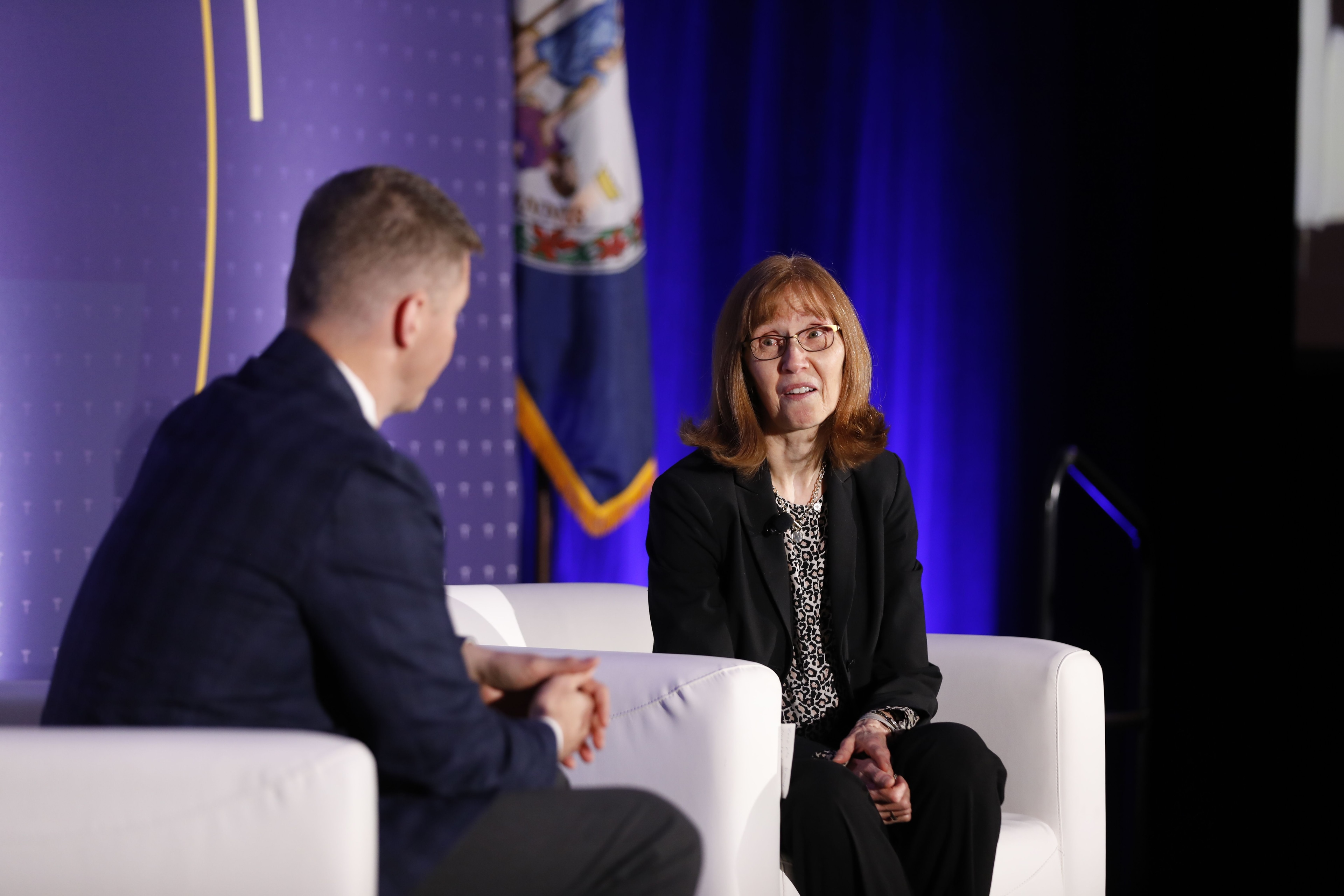 Two people in conversation on a stage with blue lighting at a government conference