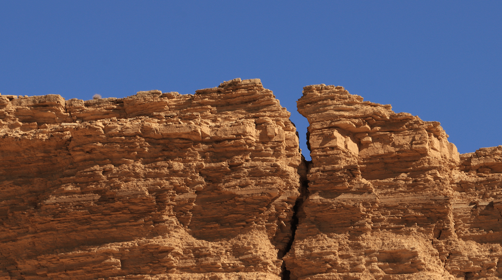 La foto di una grande crepa verticale in una parete rocciosa sotto un cielo azzurro brillante.