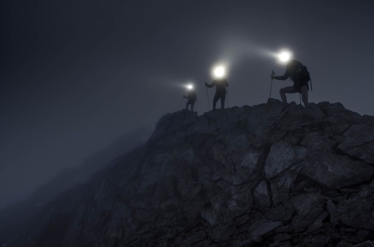 Silhouettes of figures climbing rocky mountain at night with headlamps