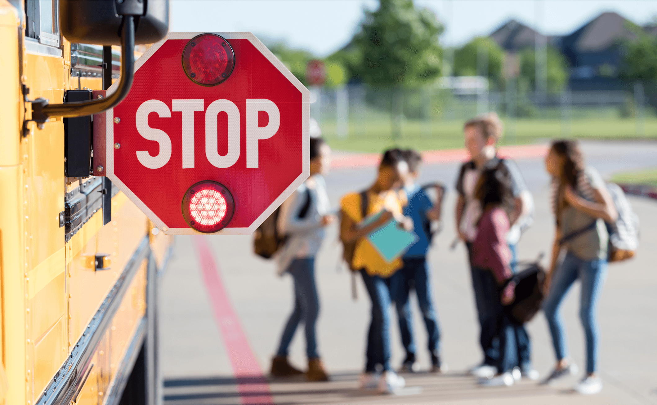 Immagine in evidenza del blog. Foto di un cartello di STOP che sporge dal lato di uno scuolabus, con studenti delle medie che chiacchierano sfocati nelle vicinanze.