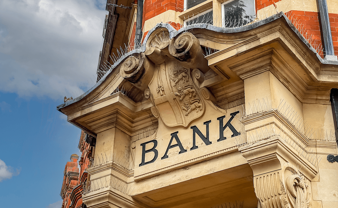 La facciata in pietra di una banca britannica, con elaborate decorazioni a volute e la parola "Bank" incisa sopra l'ingresso.