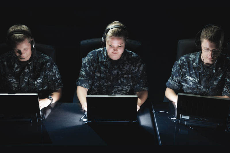 Tre membri della Marina in divisa al lavoro davanti ai computer