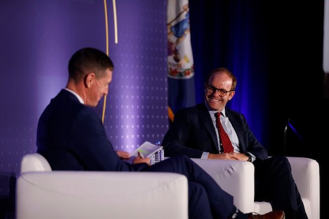 Two men in conversation on a stage with blue lighting at a government conference