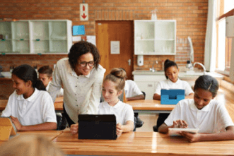 Insegnante che assiste gli studenti ai banchi con un tablet in classe