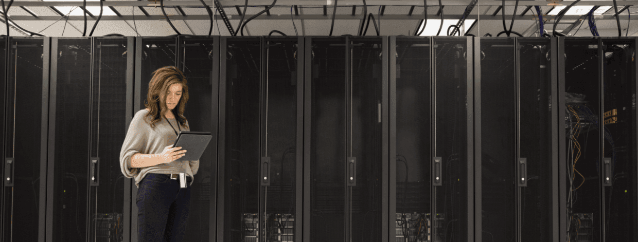 stock image: woman with tablet computer standing in front of a large server stack