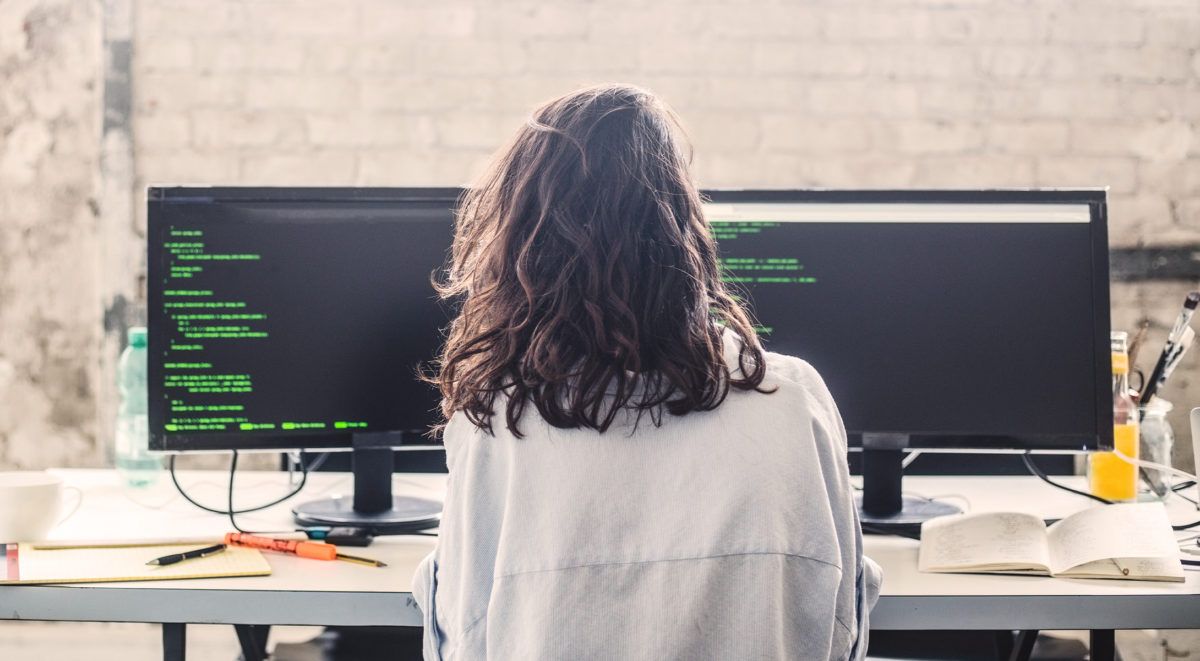 Person working at desk with dual monitors displaying code