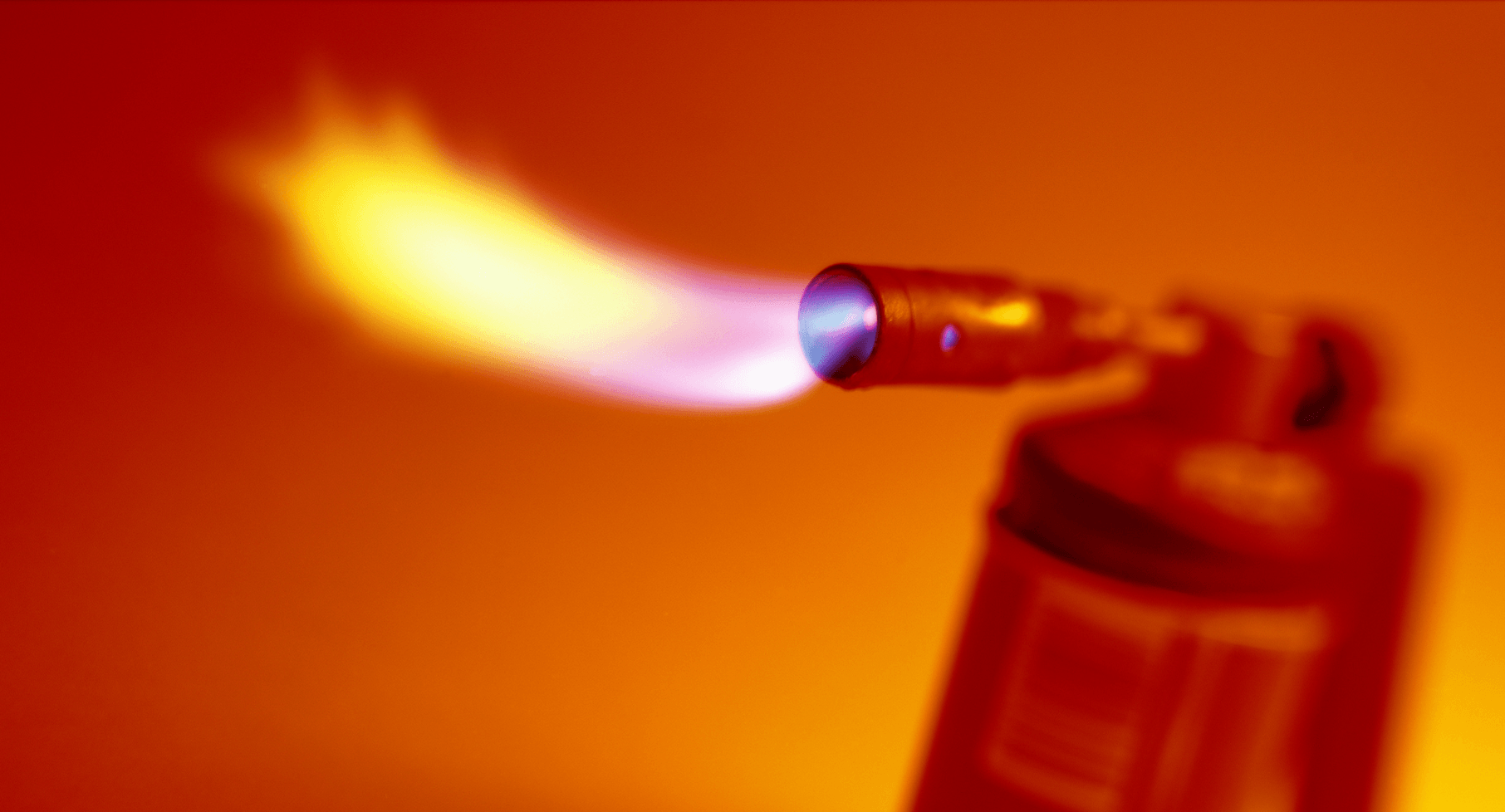 Foto di un cannello rosso che sputa fiamme, su uno sfondo arancione.
