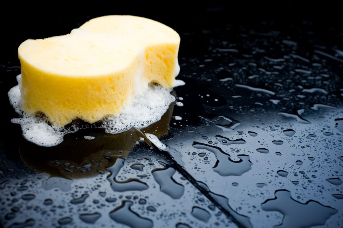 Yellow sponge on wet dark surface depicting cleaning concept