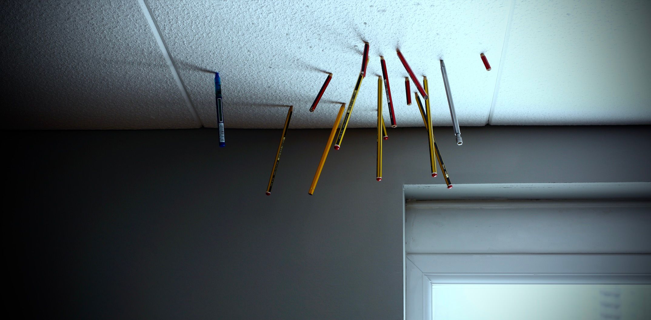 Una foto di matite conficcate in banali piastrelle del soffitto da ufficio in polistirolo.