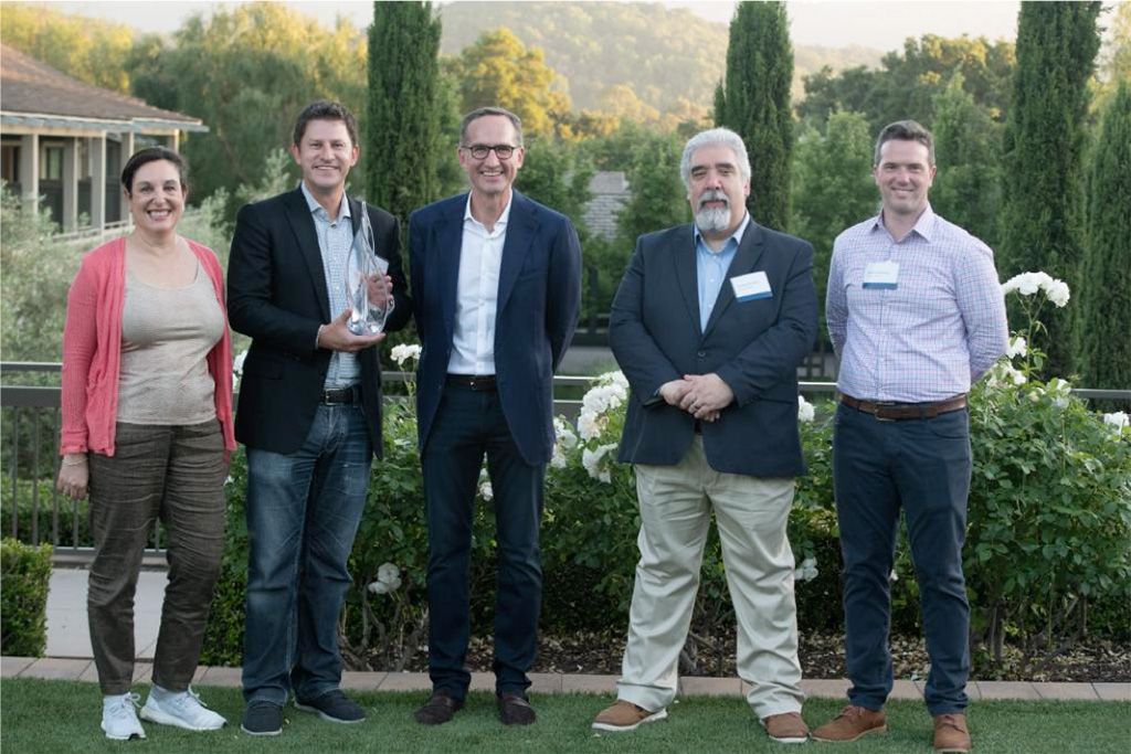 Fotografia di cinque persone durante una cerimonia di premiazione, con uno scenario all’aperto sullo sfondo