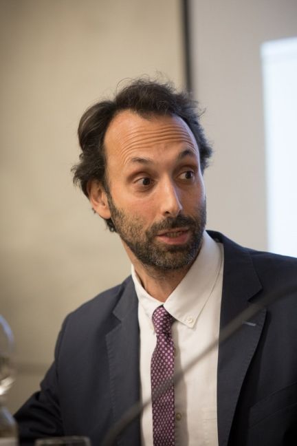 Primo piano di un uomo con la barba che indossa un abito scuro e una cravatta a motivi viola