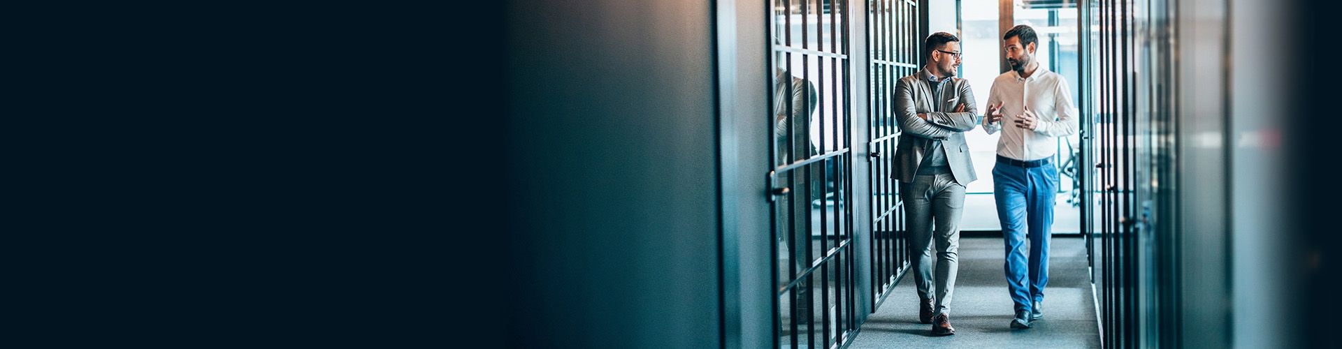 Two professionals walking in a modern glass-walled corridor
