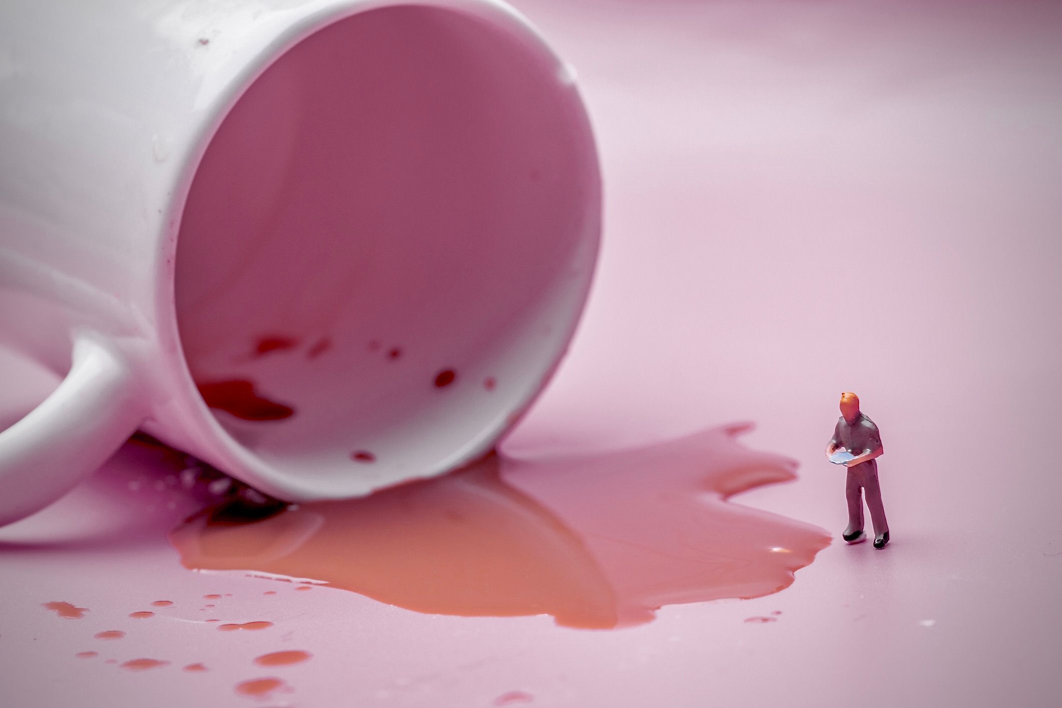 L'immagine di una figura umana in miniatura che valuta del caffè versato da una tazza rovesciata.