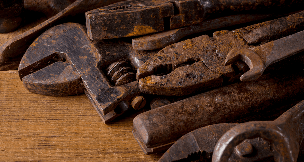 An old rusted wrench, hammer, plyers and other tools lay on a dirty metal surface.